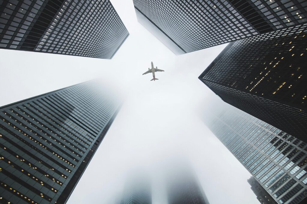 Airplane soaring above fog-enshrouded skyscrapers in an urban setting.
