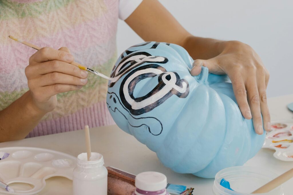 pexels-photo-5545658-5545658 Person painting a blue pumpkin with artistic designs, perfect for fall decoration and Halloween crafts.